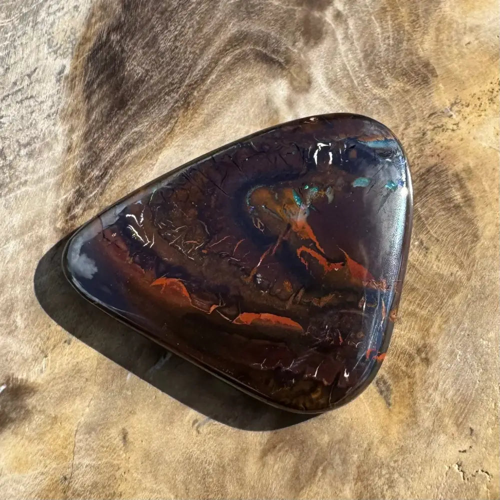 Polished, dark brown gemstone with red and blue inclusions.
