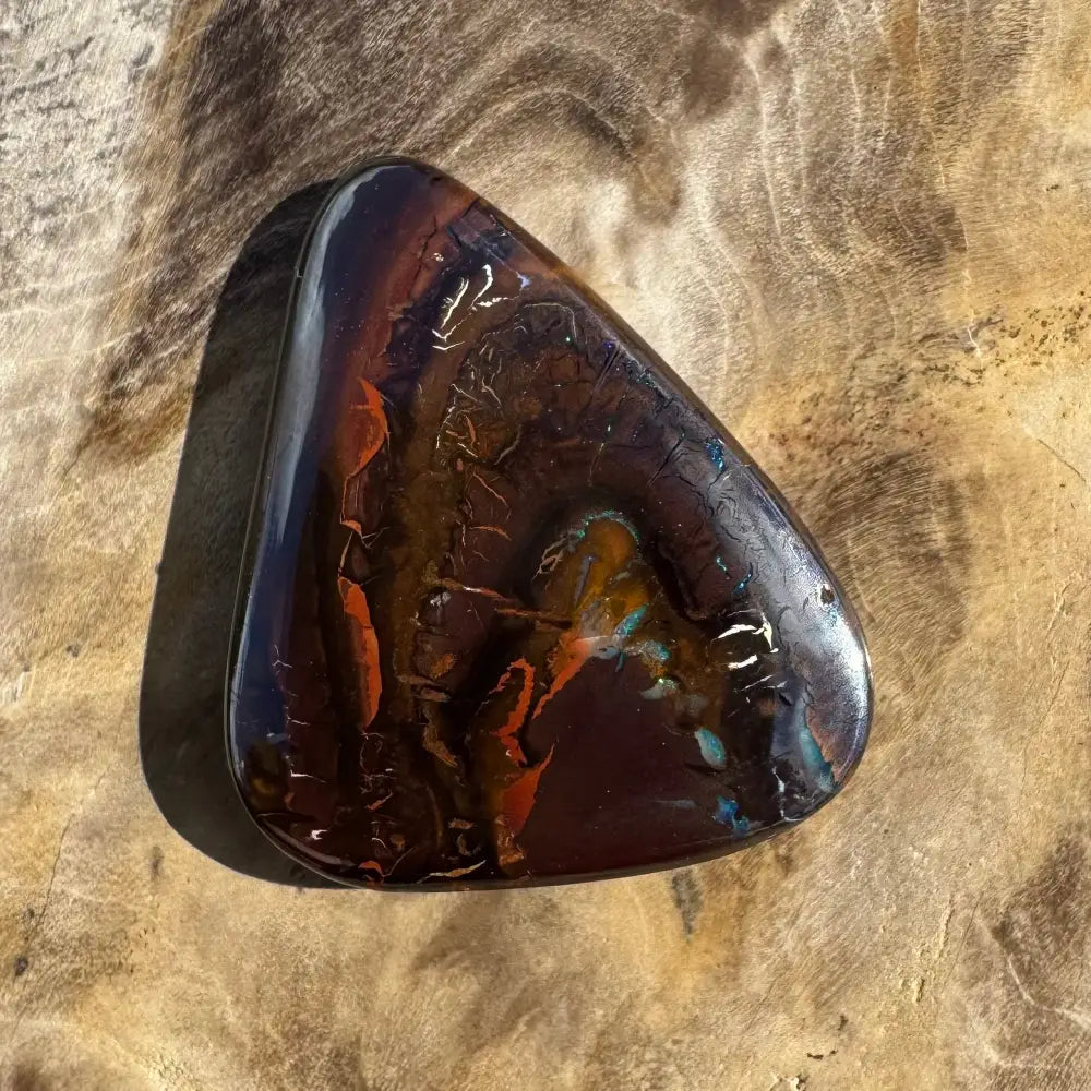 Polished, dark-toned opal cabochon with vibrant color flashes.