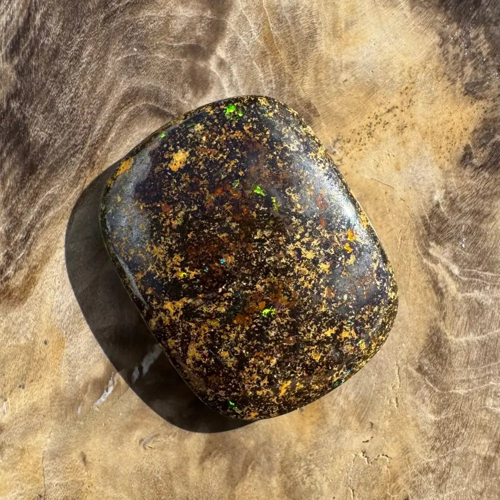 Polished black opal with gold and green flecks.