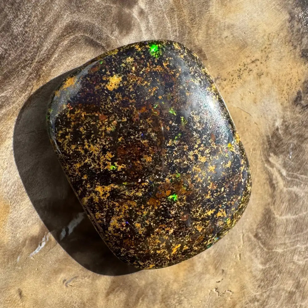 Polished black opal with gold and green flecks.