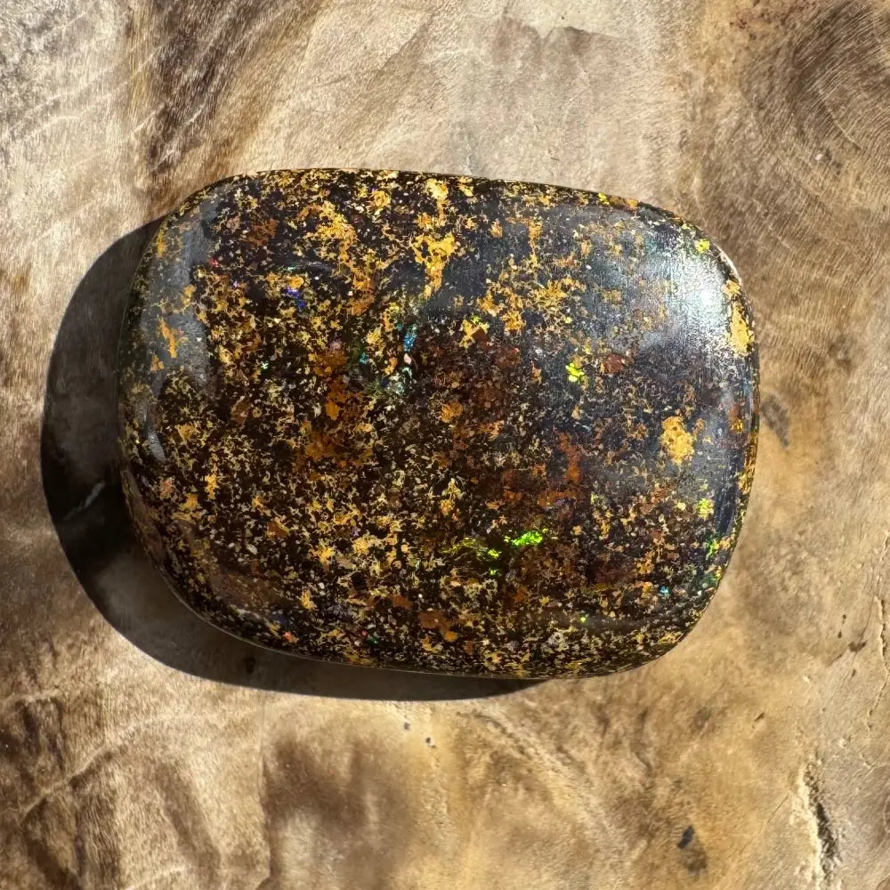 Polished black opal with gold and green flecks.