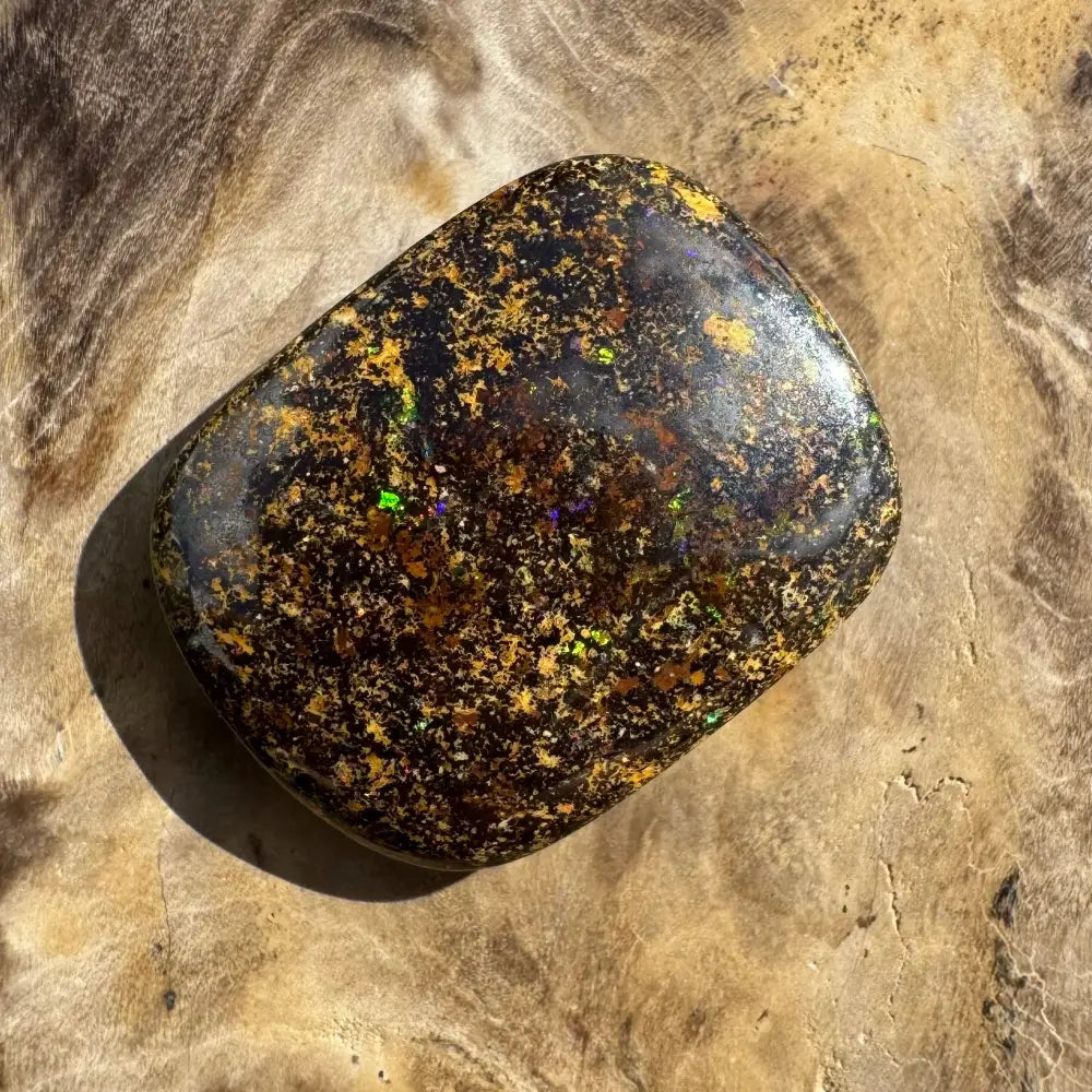 Polished black opal with gold and iridescent flecks.