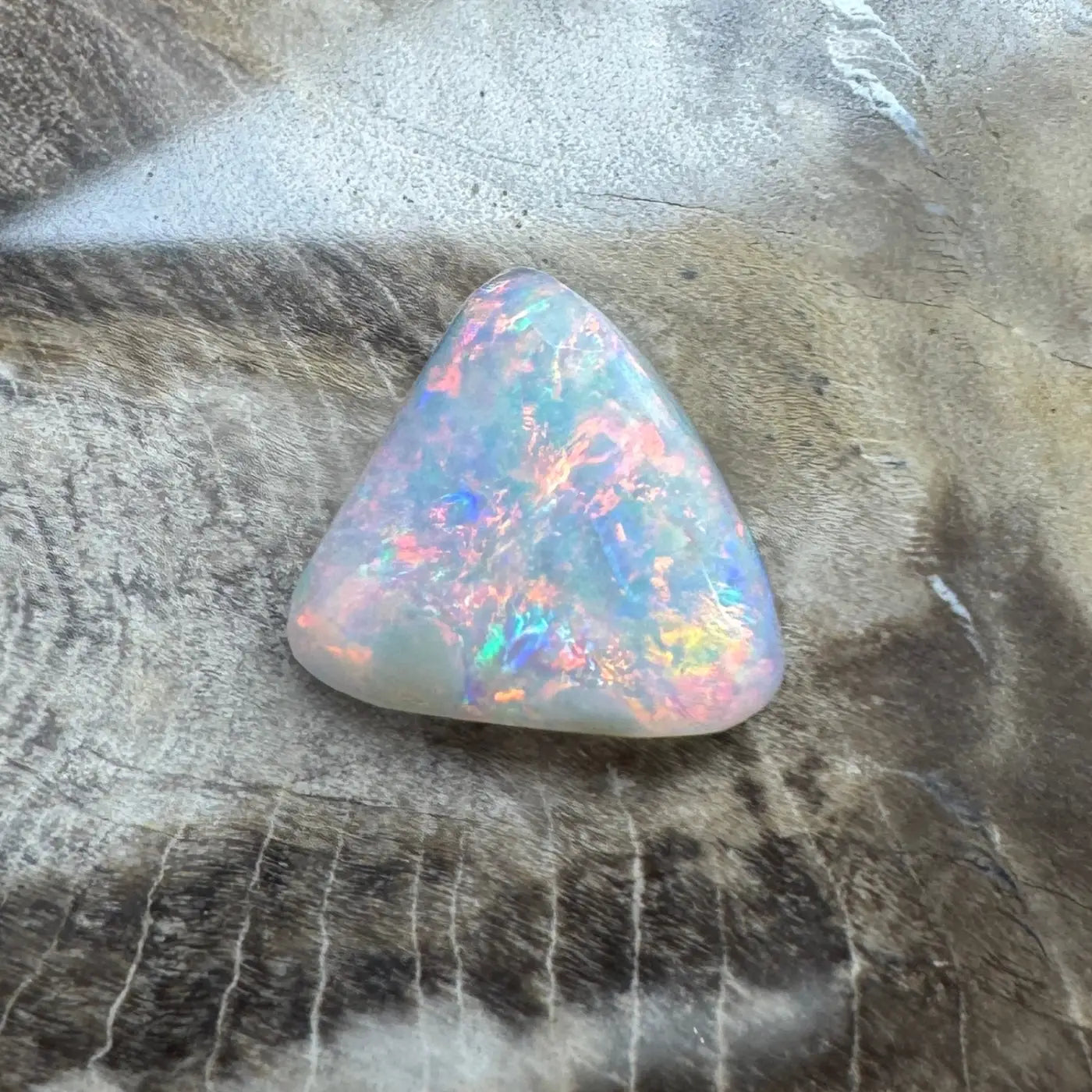 Triangular Lightning Ridge Opal gemstone with iridescent colors and a polished finish